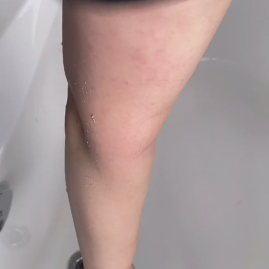 Woman demonstrating exfoliating mitt kessa scrub glove on leg for self-tanning preparation and shower
